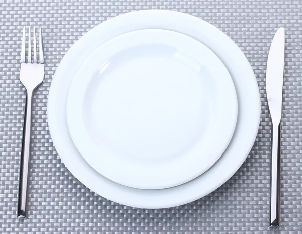 Białe puste talerze z widelcem i nożem na szary Obrus — Zdjęcie stockowe