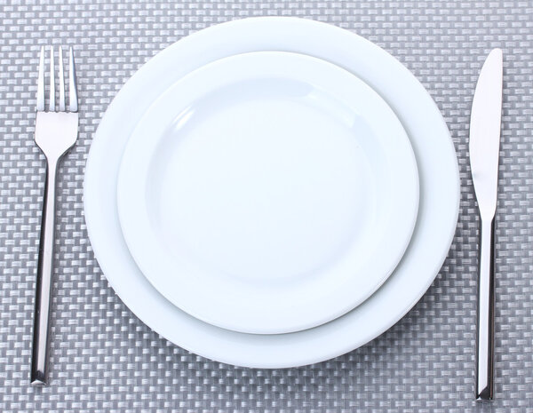 Белые пустые тарелки с вилкой и ножом на серой скатерти
