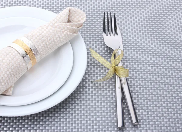 Bílé prázdné talíře s vidličkou a nožem svázané stuhou na šedé ubrus — Stock fotografie