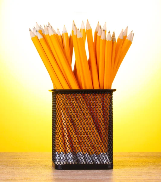 Bleistifte im Metallbecher auf Holztisch auf gelbem Hintergrund — Stockfoto
