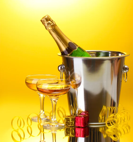 Botella de champán en cubo con hielo y copas de champán, sobre fondo amarillo — Foto de Stock