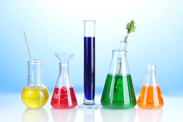 Verschiedene Laborgläser mit Farbflüssigkeit auf blauem Hintergrund — Stockfoto