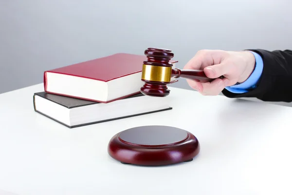 Wooden gavel in hand and books on gray background — Stock Photo, Image