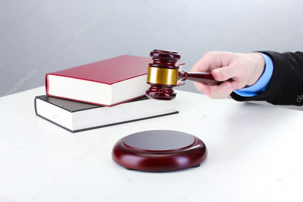 Wooden gavel in hand and books on gray background