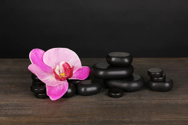 Piedras de spa con flor de orquídea sobre mesa de madera sobre fondo gris —  Fotos de Stock