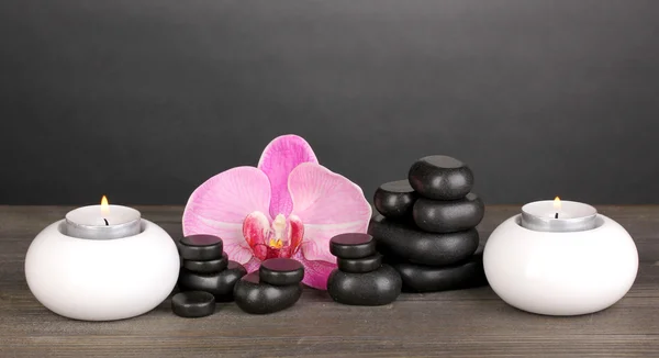 Piedras de spa con flor de orquídea y velas sobre mesa de madera sobre fondo gris —  Fotos de Stock