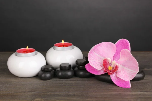 Wellness-Steine mit Orchideenblume und Kerzen auf Holztisch auf grauem Hintergrund — Stockfoto