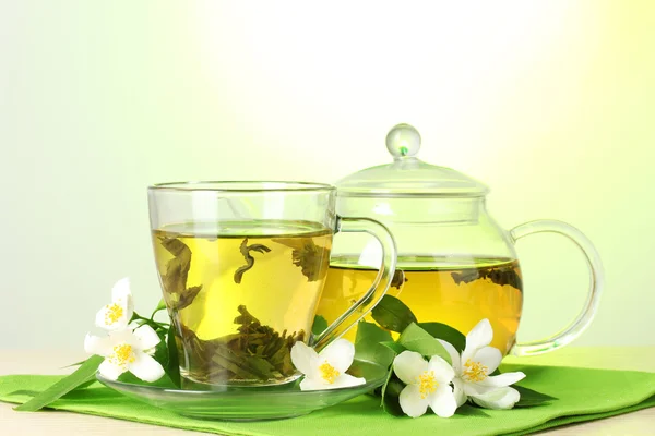 Herbata zielona z jaśminu w Pucharze i czajnik na drewnianym stole na zielonym tle — Zdjęcie stockowe