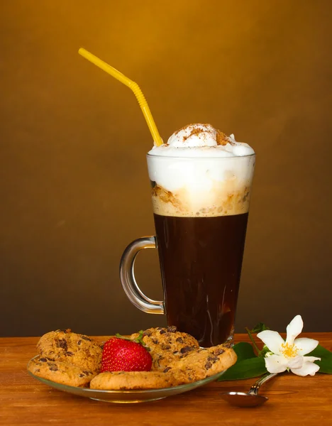 Стакан кофе с печеньем и клубникой на блюдце и цветок на коричневом фоне — стоковое фото