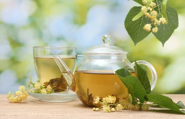 Teiera e tazza con tiglio tè e fiori su tavolo in legno in giardino — Foto Stock