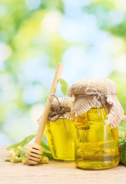 Баночки с липовым медом и цветы на деревянном столе на зеленом фоне — стоковое фото