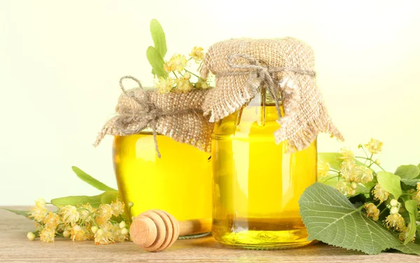 Bocaux au miel de tilleul et fleurs sur table en bois sur fond vert — Photo