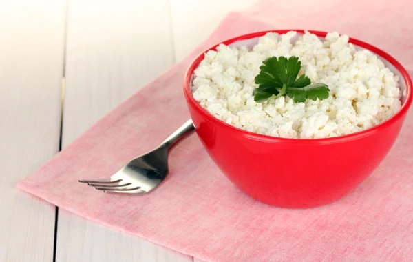 Cottage cheese with parsley in red bowl and fork on pink napkin on white wooden table close-up — Stock Photo, Image