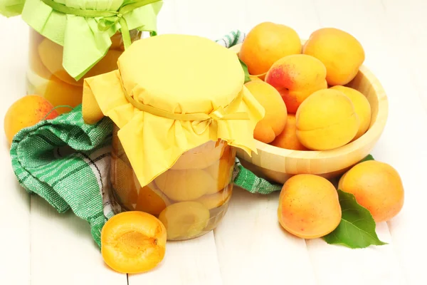 Konserverade aprikoser i en burkar och mogna aprikoser i skål på vita träbord — Stockfoto