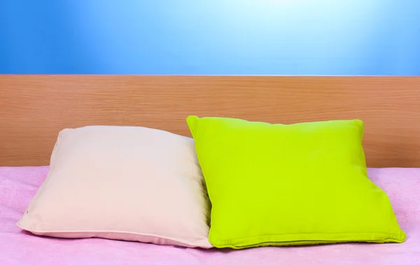 Almofadas brilhantes na cama no fundo azul — Fotografia de Stock