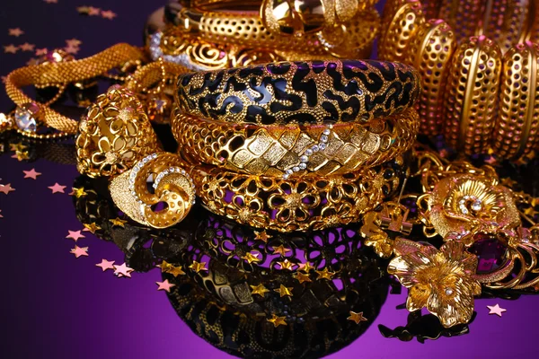Hermosa joyería dorada sobre fondo púrpura — Foto de Stock