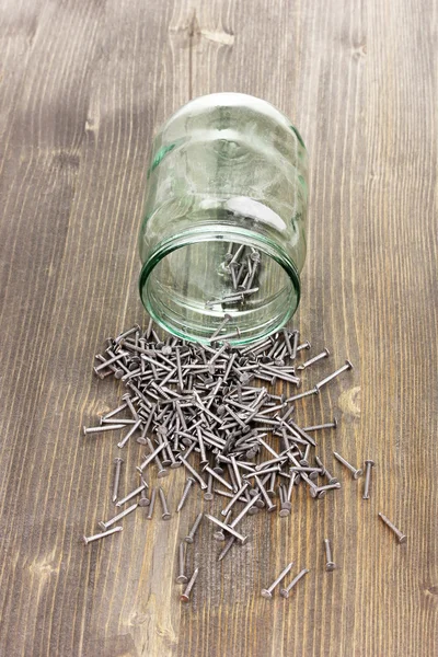 Pregos de metal e frasco de vidro no fundo de madeira — Fotografia de Stock