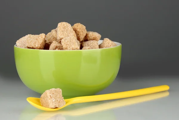 Barevná miska s hnědý třtinový cukr kostky barevné lžící na šedém pozadí detail — Stock fotografie