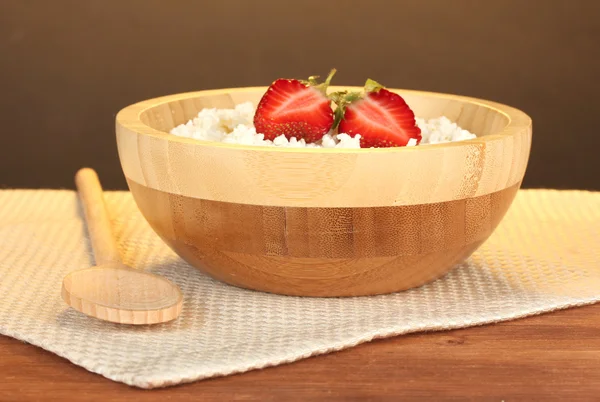 Requesón con fresa en cuenco de madera con cuchara de madera sobre servilleta beige sobre mesa de madera sobre fondo marrón — Foto de Stock