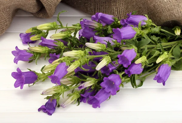 Mavi çan çiçekleri ve Beyaz ahşap zemin üzerine çuval bezi — Stok fotoğraf