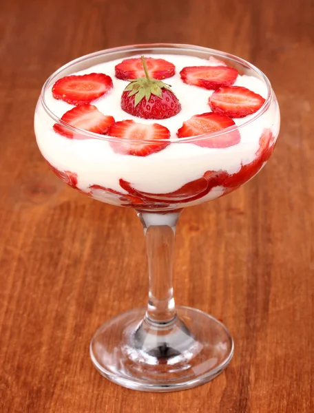 Glas van rijpe aardbeien met crème op houten achtergrond — Stockfoto