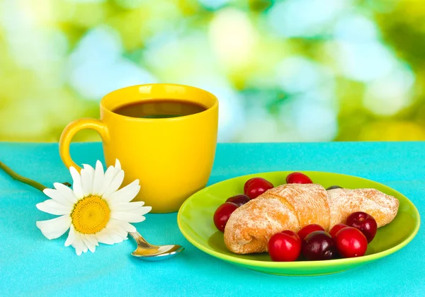 Croissant mit Kirschen und Kaffee auf Holztisch auf grünem Hintergrund — Stockfoto