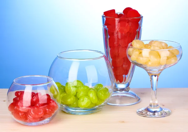 Farbbonbons in Gläsern auf Holztisch auf blauem Hintergrund — Stockfoto