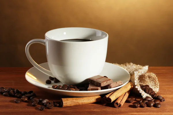 Taza de café y frijoles, palitos de canela y chocolate sobre mesa de madera sobre fondo marrón —  Fotos de Stock