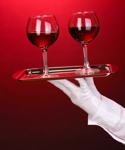 Hand in glove holding silver tray with wineglasses on red background — Stock Photo, Image