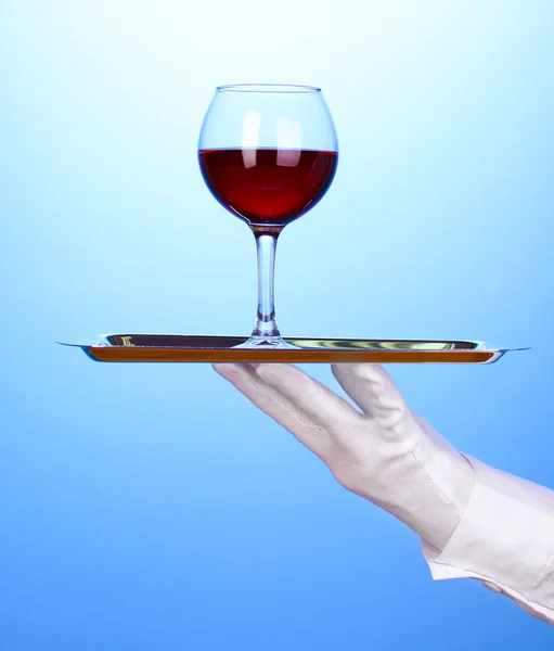 Hand in glove holding silver tray with wineglass on blue background — Stock Photo, Image