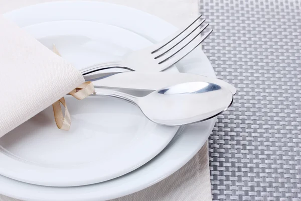 Platos blancos vacíos con tenedor, cuchara y cuchillo atados con una cinta sobre un mantel gris — Foto de Stock