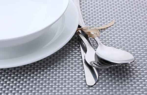 Witte lege platen met mes, lepel en vork gebonden met een lint op een grijze tafellaken — Stockfoto