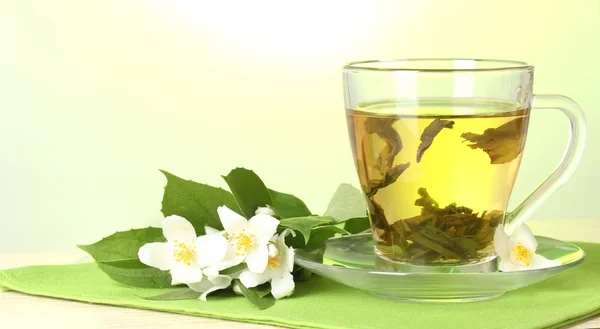 Чашка зеленого чаю з квітами жасмину на дерев'яному столі на зеленому фоні — стокове фото