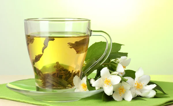 Tasse grüner Tee mit Jasminblüten auf Holztisch auf grünem Hintergrund — Stockfoto