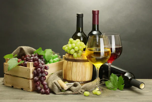 Бочка, бутылки и бокалы вина и спелый виноград на деревянном столе на сером фоне — стоковое фото