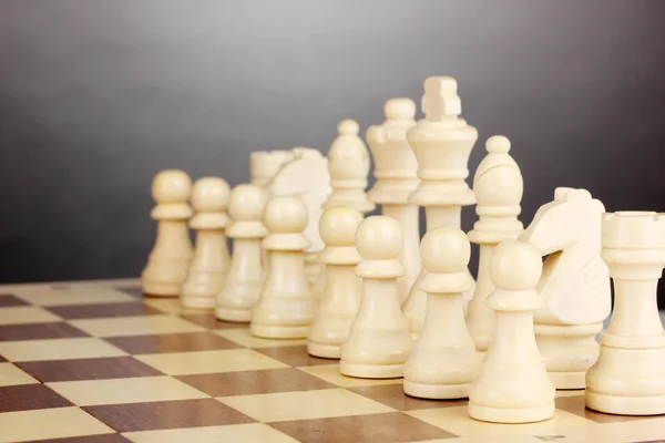 Gri arka plan üzerinde satranç taşları ile satranç masası — Stok fotoğraf