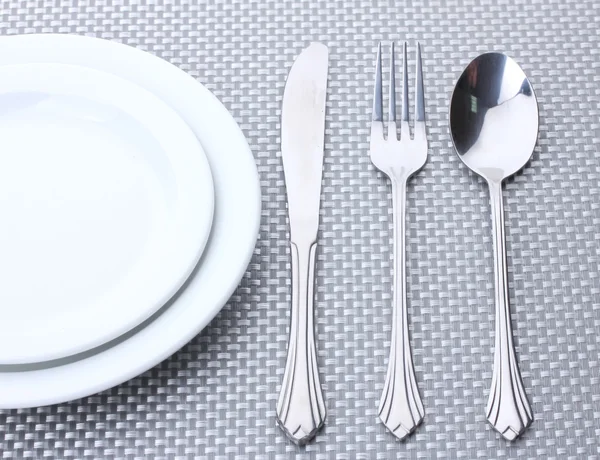 Bílé prázdné talíře, vidlička, lžíce a nůž na šedé ubrus — Stock fotografie
