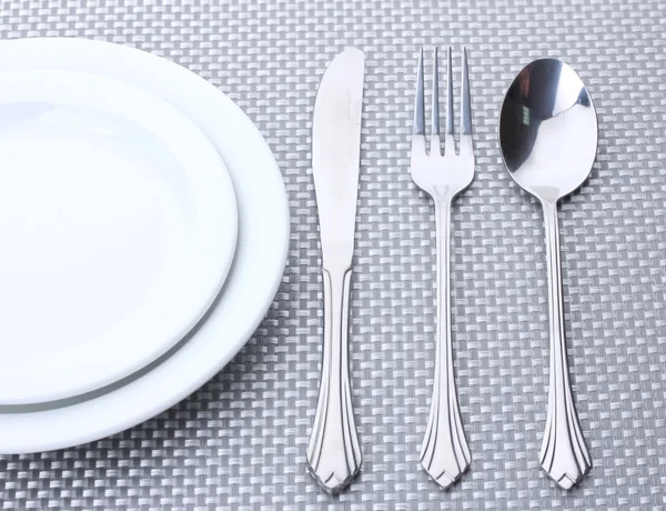 Platos blancos vacíos con tenedor, cuchara y cuchillo sobre un mantel gris —  Fotos de Stock