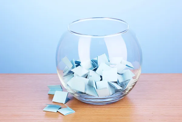 Pièces de papier pour loterie dans un vase sur une table en bois sur fond bleu — Photo