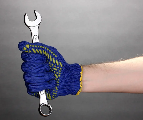 Ключ в руке с защитной перчаткой на сером фоне — стоковое фото