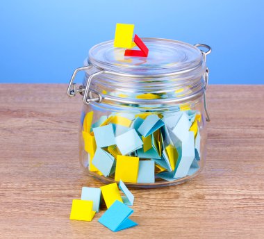 Pieces of paper for lottery in jar on wooden table on blue background clipart