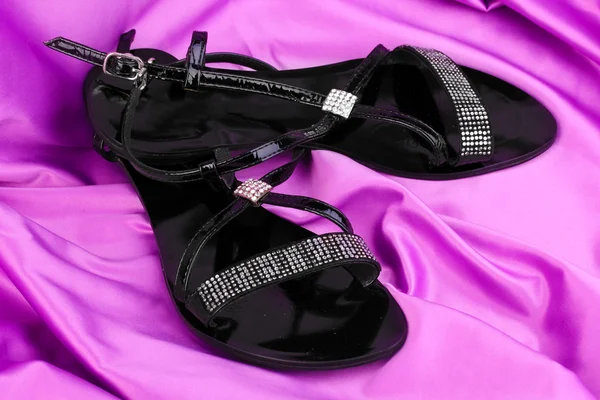 Schwarze Sandalen auf lila Tuch — Stockfoto