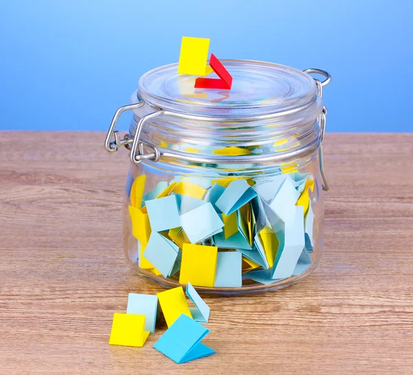 Stukjes papier voor loterij in pot op houten tafel op blauwe achtergrond — Stockfoto