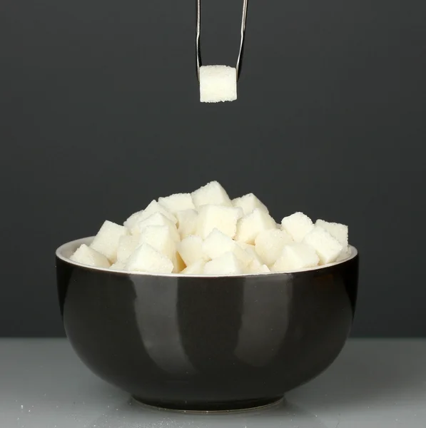 White lump sugar in bowl with sugar-tongs on grey background — Stock Photo, Image