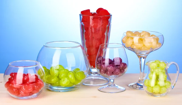 Farbbonbons in Gläsern auf Holztisch auf blauem Hintergrund — Stockfoto