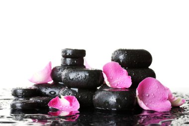 Spa stones with drops and rose petals on white background