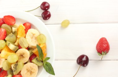 Fresh fruits salad on plate and berries on white wooden table clipart