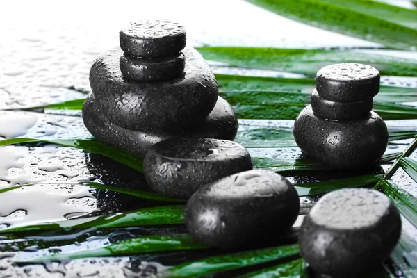 Piedras de spa con gotas en hoja de palma verde sobre fondo gris —  Fotos de Stock