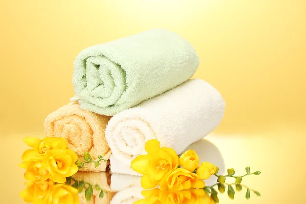Kleurrijke handdoeken en bloemen op gele achtergrond — Stockfoto