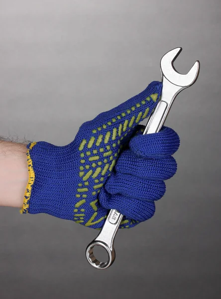 Schraubenschlüssel in der Hand mit Schutzhandschuh auf grauem Hintergrund — Stockfoto